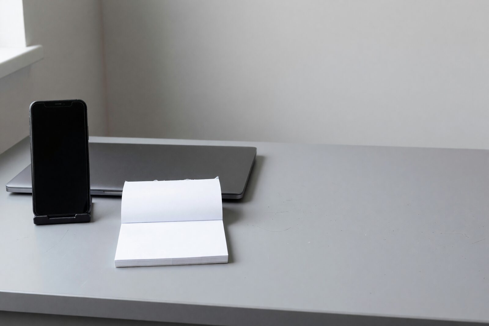 Illustration: a phone in a stand on a desk, beside an open notepad and a closed laptop.