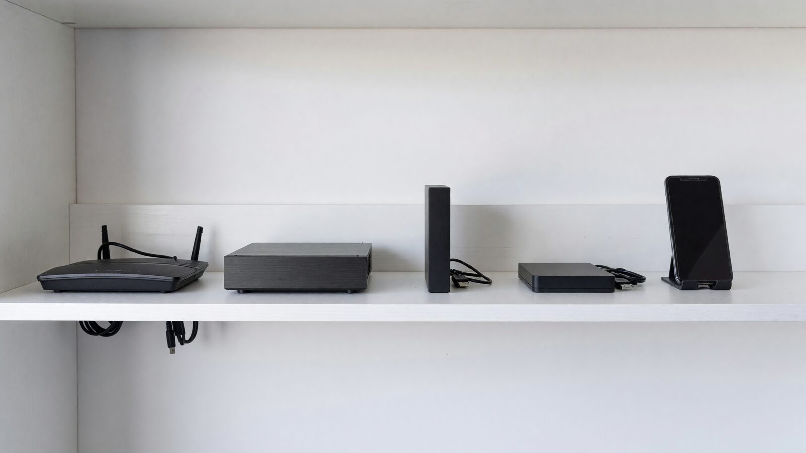 Illustration: an office shelf with a router, a small server, an upright drive, a backup drive and a phone on a stand.